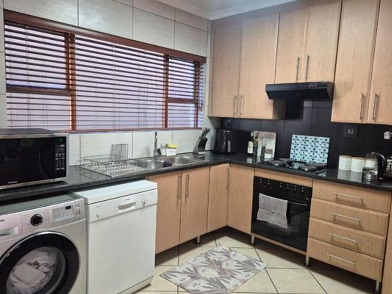 A functional kitchen featuring light wood cabinetry, dark countertops, tiled backsplash, and integrated appliances including an oven, hob, and extractor fan.