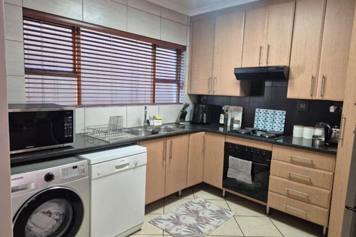 A functional kitchen featuring light wood cabinetry, dark countertops, tiled backsplash, and integrated appliances including an oven, hob, and extractor fan.