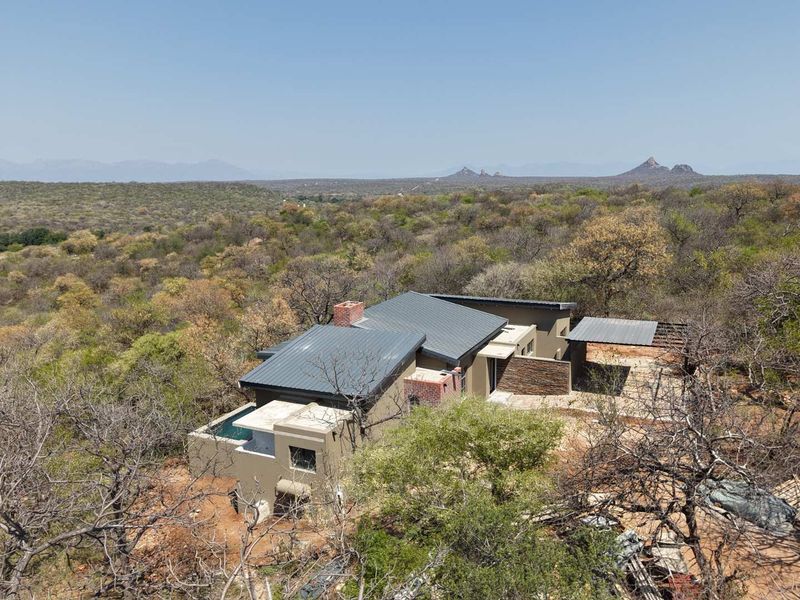 Aerial view of a modern residence featuring a metal roof, stone accents, and a swimming pool, set within a natural bushveld landscape.