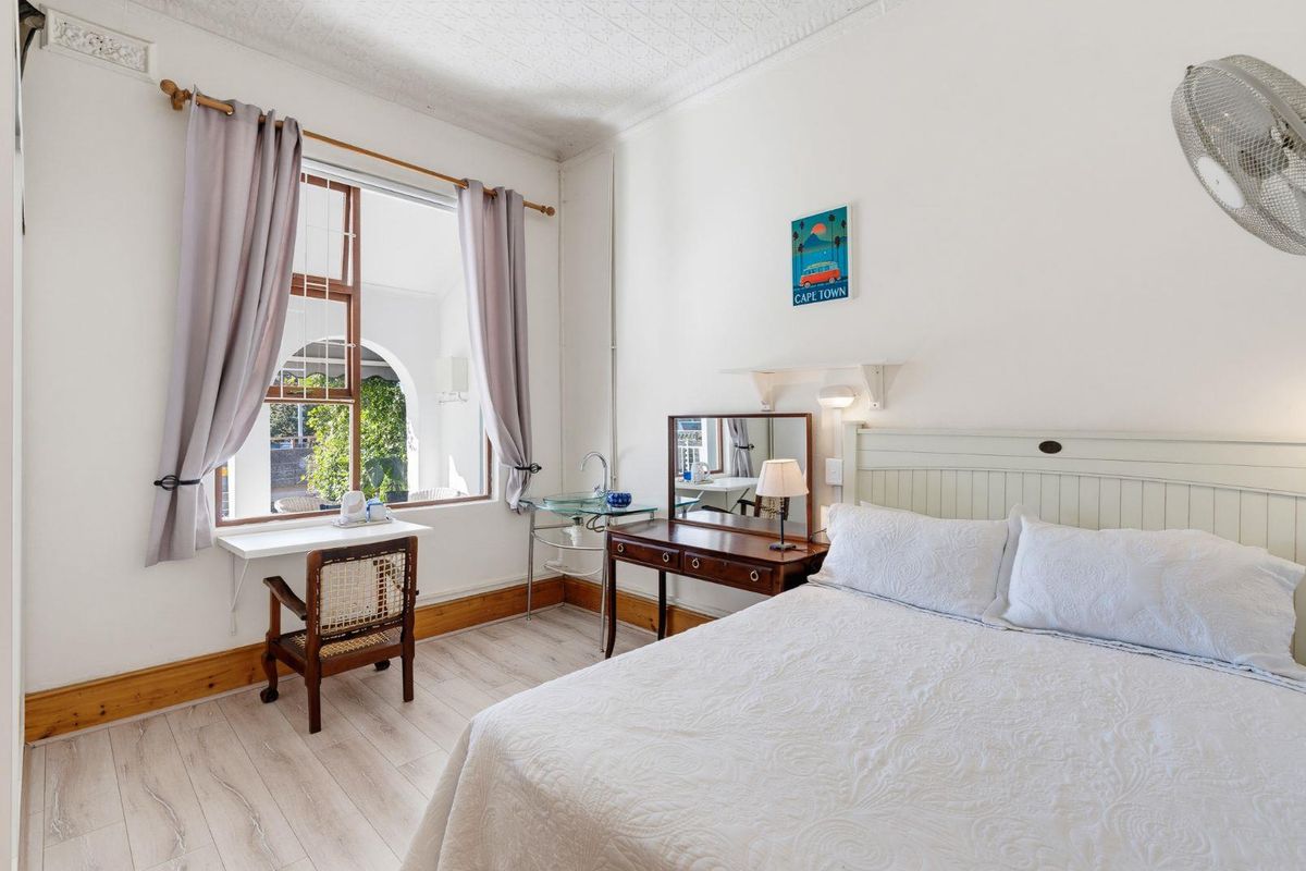 A bright bedroom featuring light-toned laminate flooring, decorative ceiling cornices, and a convenient wall-mounted basin, with direct access to an outdoor patio area.