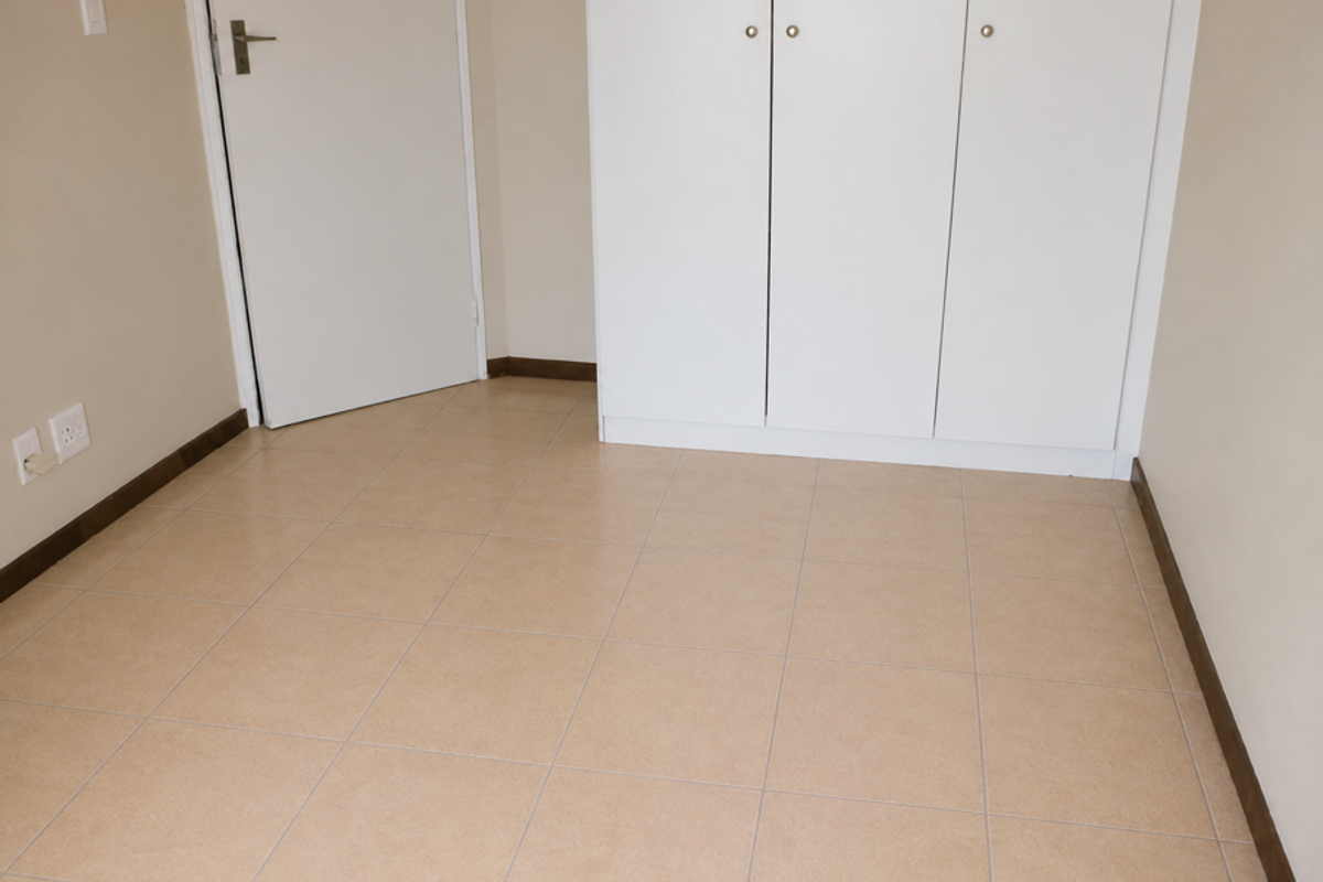 A clean, empty bedroom featuring neutral floor tiles, built-in white cabinetry, and a standard interior door.
