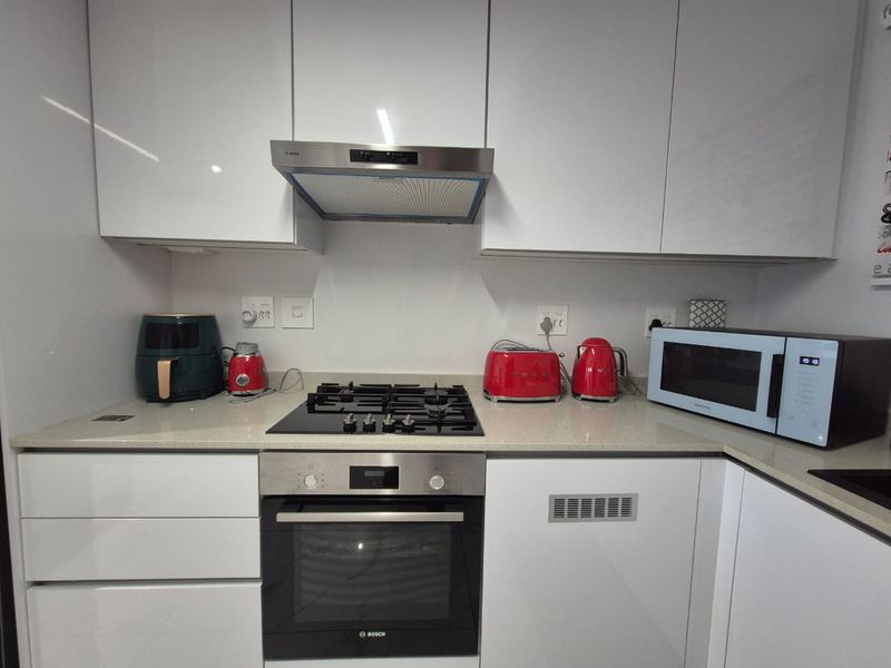 Modern kitchen featuring white high-gloss cabinetry, stone countertops, and integrated Bosch appliances including a gas cooktop, oven, and extractor fan.