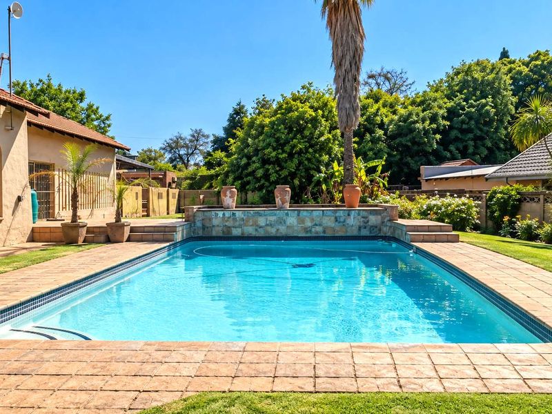 A well-maintained swimming pool area featuring a stone-clad water feature, paved surround, and established garden borders.