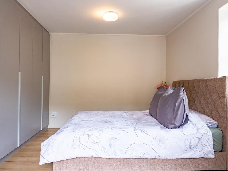 A well-maintained bedroom featuring modern built-in cupboards, light laminate flooring, and a neutral color palette.