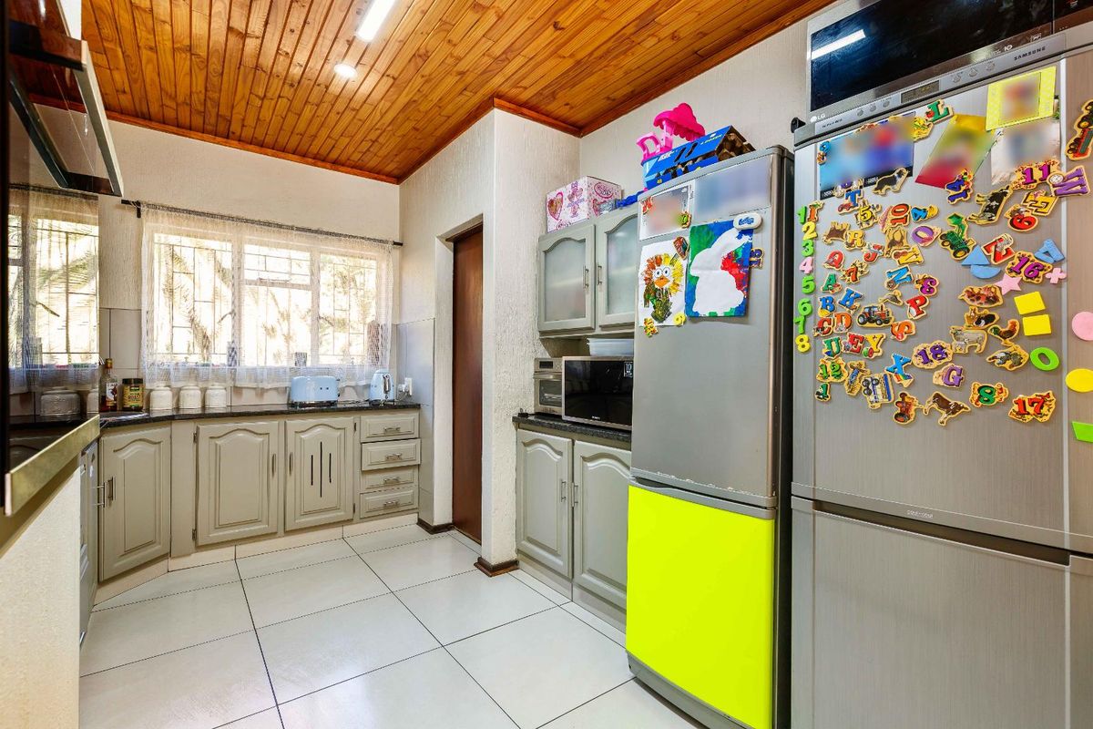 A functional kitchen featuring light-toned cabinetry, dark countertops, tiled flooring, and a distinctive timber-paneled ceiling with integrated lighting.