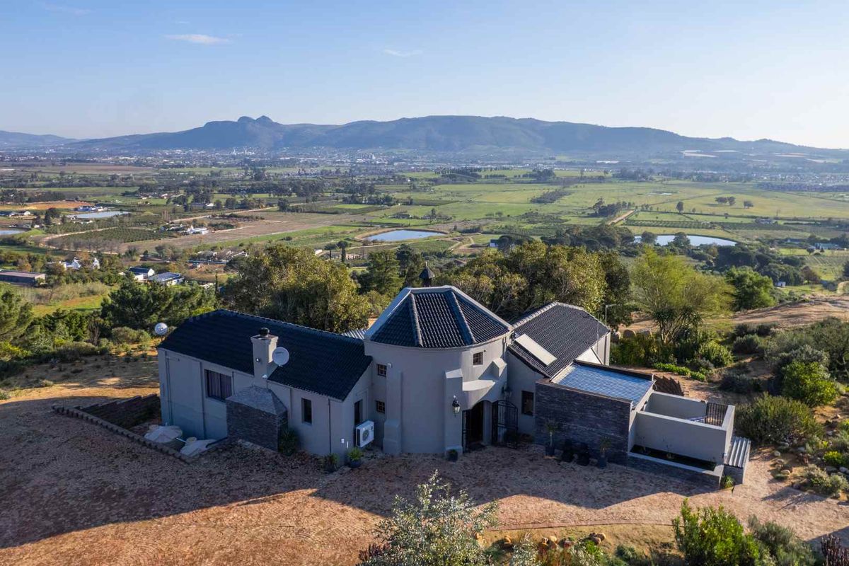Aerial view of a farm-style residence featuring a distinctive turret design, dark tiled roof, stone accents, and expansive rural landscape views.