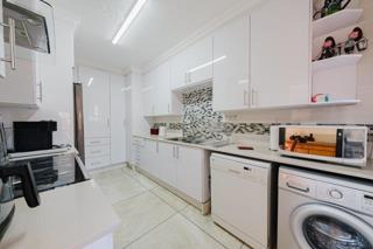 Modern kitchen featuring glossy white cabinetry, stone countertops, a mosaic tile backsplash, and integrated appliances in a clean, functional layout.