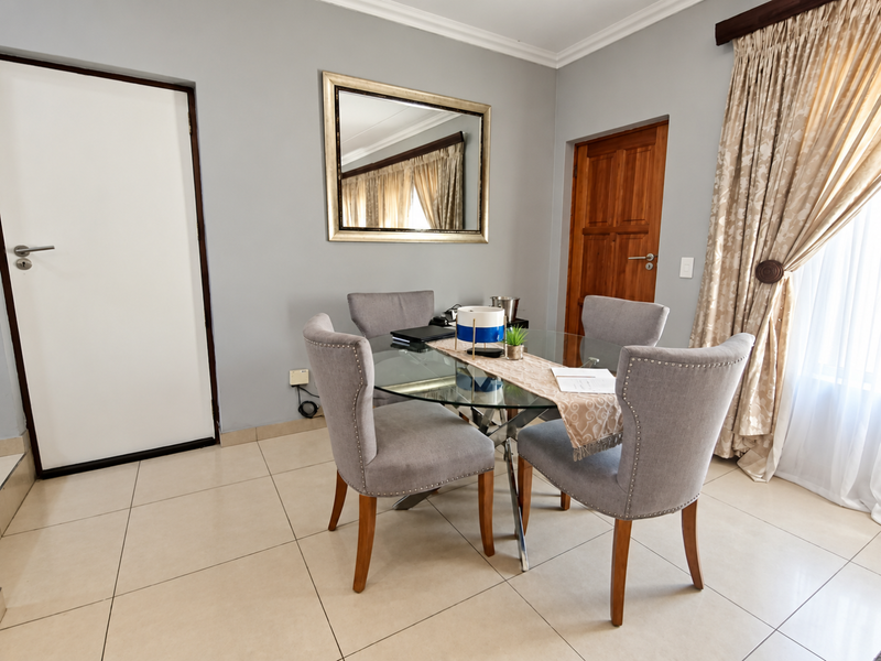 A well-maintained dining area featuring neutral tiled flooring, coving, and a solid timber door, providing a clean and functional space for meals.