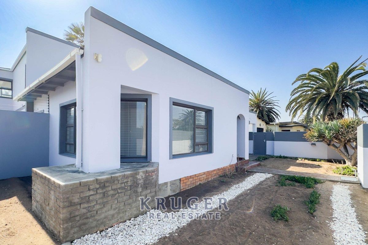 Rear exterior view of the property featuring modern white facade, aluminium window frames, and a low-maintenance gravel garden area.