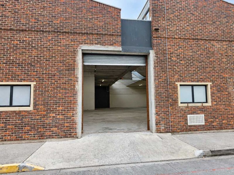 Industrial property exterior featuring a brick facade, concrete driveway access, and a large roller shutter door entrance.