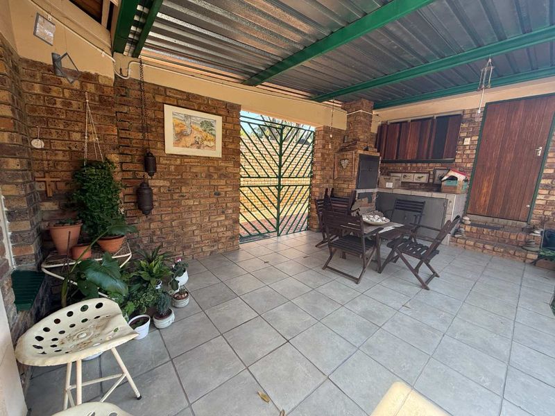 Covered outdoor patio area featuring a built-in braai, tiled flooring, and exposed brick walls, providing a functional space for outdoor entertaining.