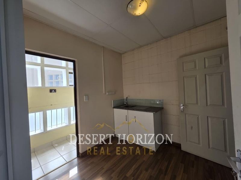 A compact kitchenette area featuring a small sink, tiled backsplash, and laminate flooring, suitable for a small office or utility space.