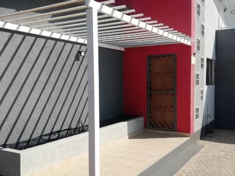 Front entrance area featuring a modern pergola, tiled patio, built-in planter, and secure entrance door with a security gate.