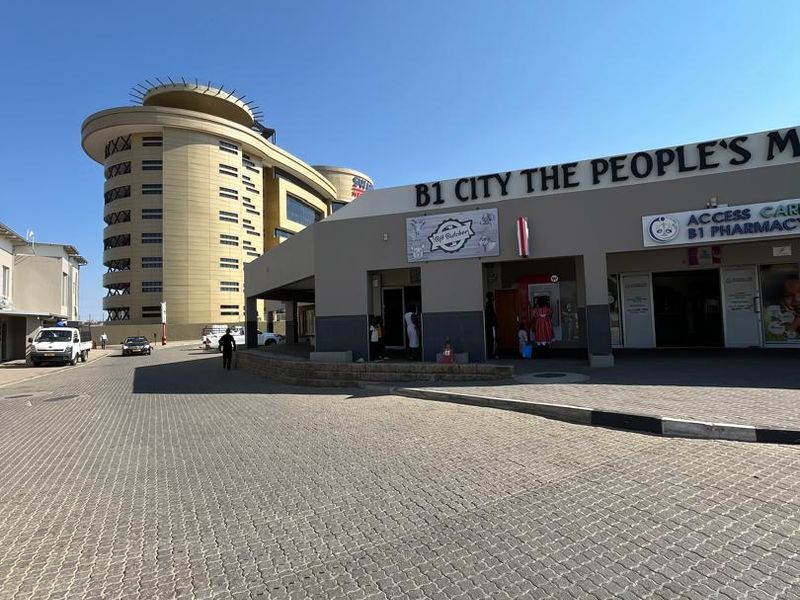 Exterior view of B1 City commercial complex featuring paved parking area, covered walkways, and prominent signage for retail units.