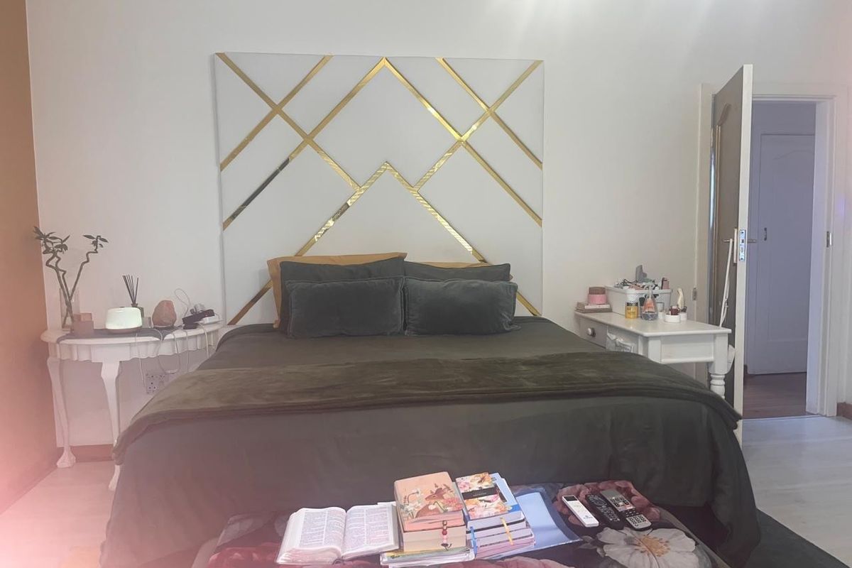 A well-maintained bedroom featuring a modern geometric gold-accented decorative wall panel behind the bed area.