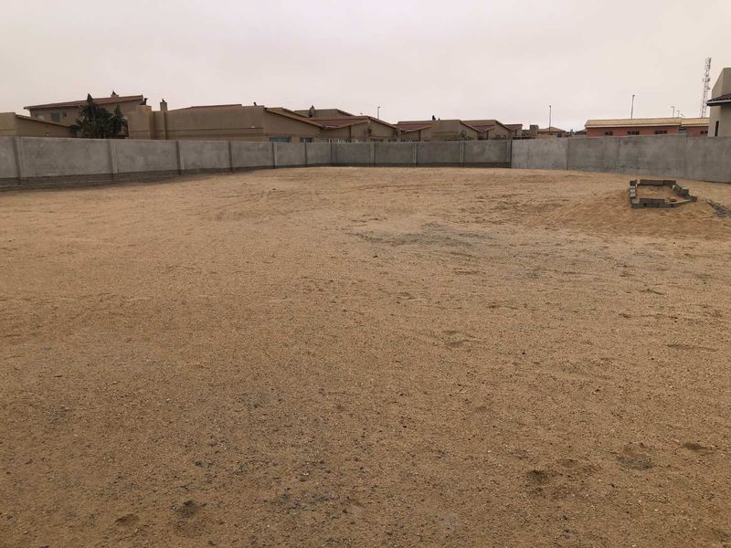 A vacant residential plot enclosed by a perimeter concrete wall, offering a blank canvas for future development.