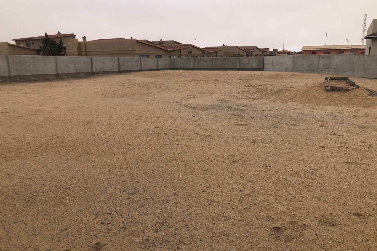 A vacant residential plot enclosed by a perimeter concrete wall, offering a blank canvas for future development.