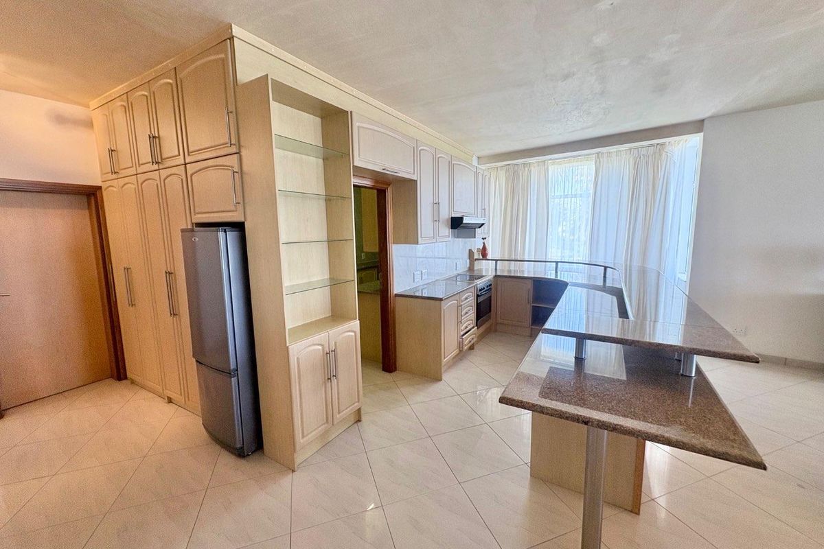 A spacious kitchen featuring light-toned cabinetry, granite countertops, a breakfast bar, and tiled flooring, offering a functional layout for cooking and dining.