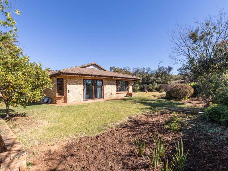 A view of the rear elevation of a face brick house featuring a tiled roof, sliding glass doors, and a surrounding garden.