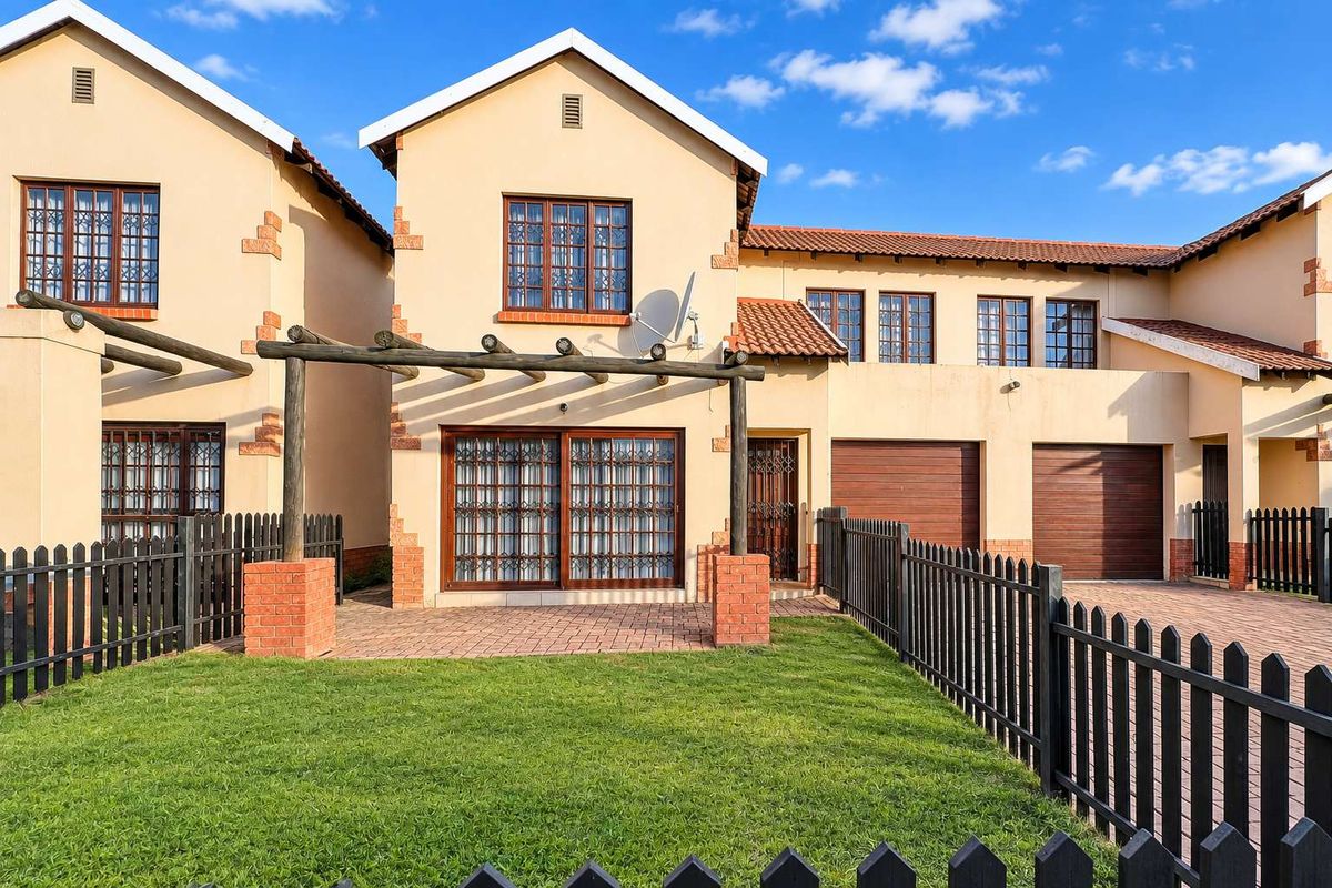 Rear view of the townhouse featuring a paved patio with a timber pergola, a private garden, and integrated garage access.