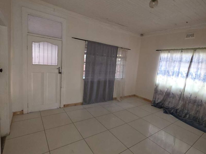 An empty living room featuring tiled flooring, a timber tongue and groove ceiling, and a classic timber panel door with glass insert.