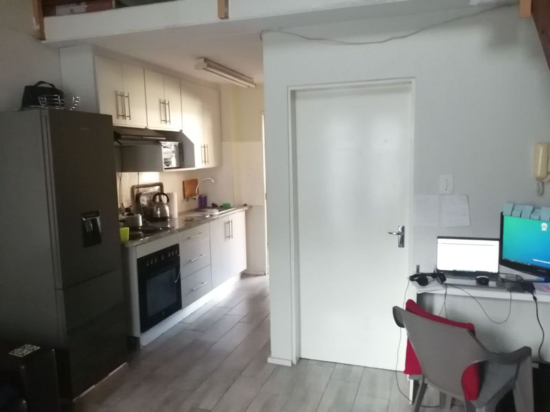 A compact kitchen area featuring built-in cabinetry, integrated oven and hob, and tiled flooring, adjacent to a small workspace area.