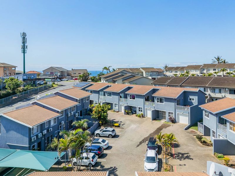 Aerial view of a residential apartment complex featuring paved parking areas, tiled roofs, and private balconies within a well-maintained estate.