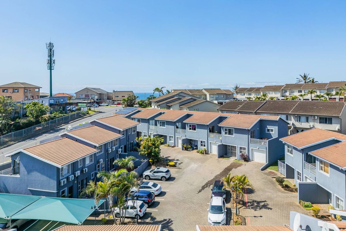 Aerial view of a residential apartment complex featuring paved parking areas, tiled roofs, and private balconies within a well-maintained estate.