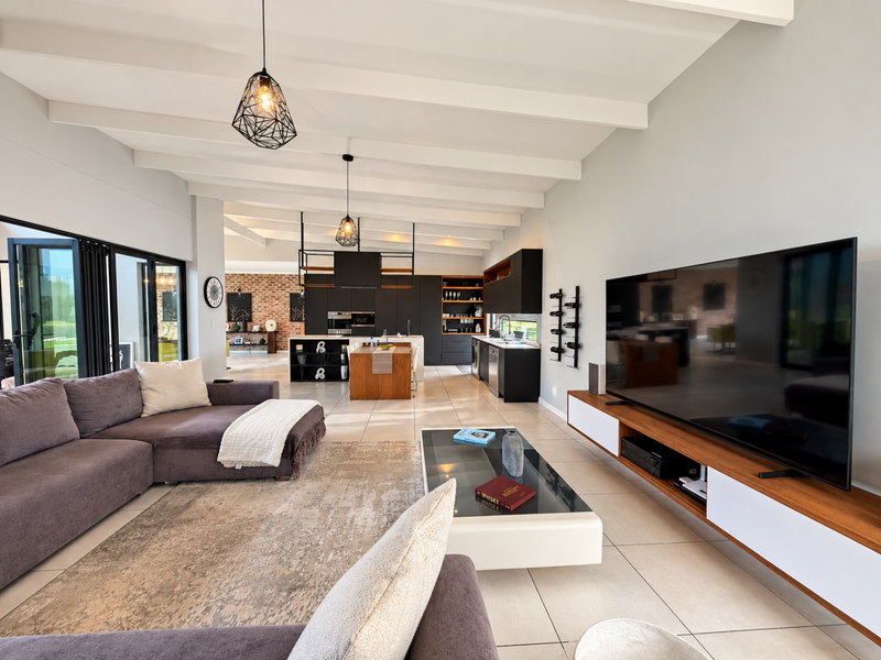 Spacious open-plan living and kitchen area featuring exposed ceiling beams, modern cabinetry, built-in appliances, and large bi-fold doors leading to the outdoors.