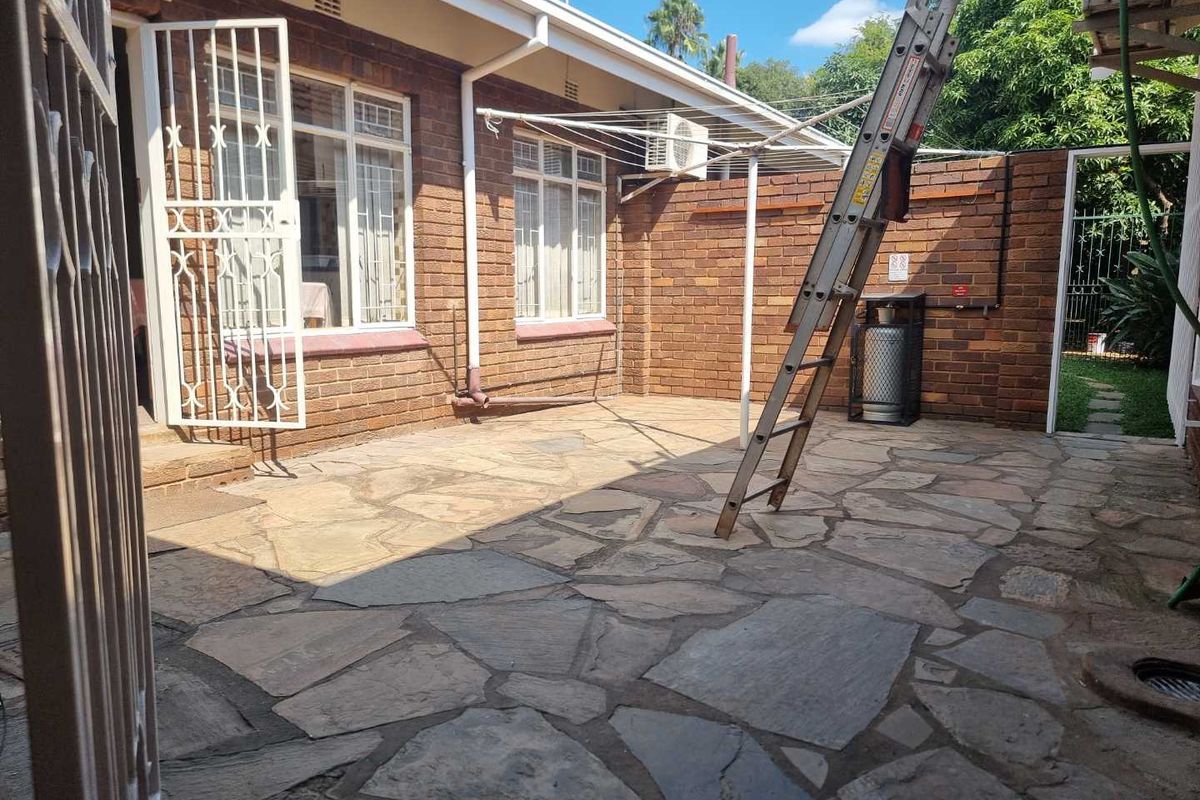 A paved rear courtyard area featuring exposed brick walls, security gates, and a wall-mounted air conditioning unit.