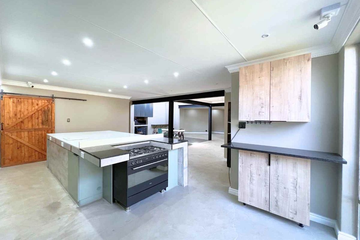 Modern open-plan kitchen featuring a large central island with a gas stove, light wood cabinetry, and industrial-style exposed steel beams.