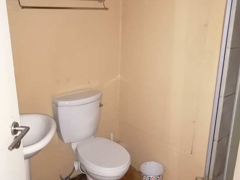 A compact bathroom featuring a standard toilet, pedestal basin, and shower enclosure, requiring cosmetic updates to improve its overall condition.