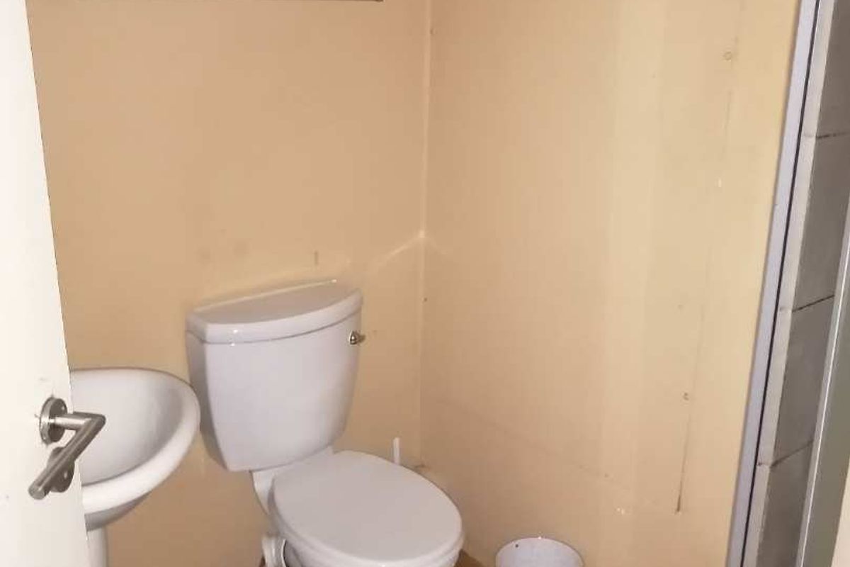 A compact bathroom featuring a standard toilet, pedestal basin, and shower enclosure, requiring cosmetic updates to improve its overall condition.