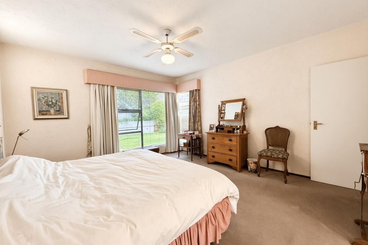 A spacious bedroom featuring neutral wall finishes, carpeted flooring, and a ceiling fan, with large windows providing natural light and garden views.