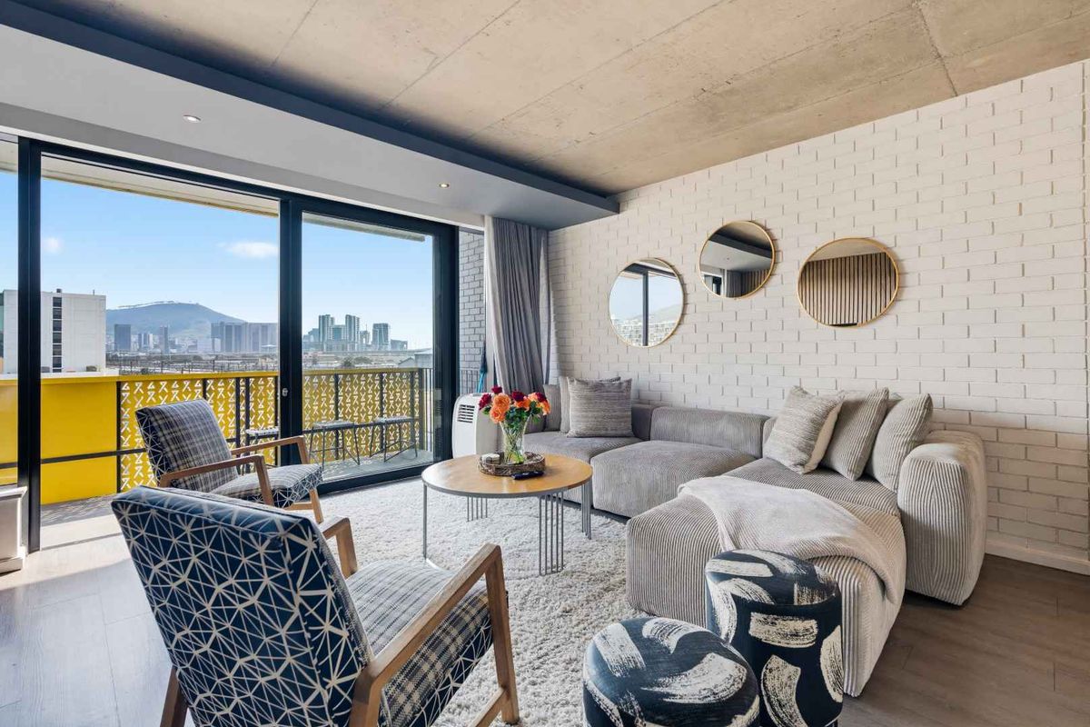 Modern living room featuring an exposed concrete ceiling, painted brick feature wall, and large sliding glass doors opening to a balcony with city views.