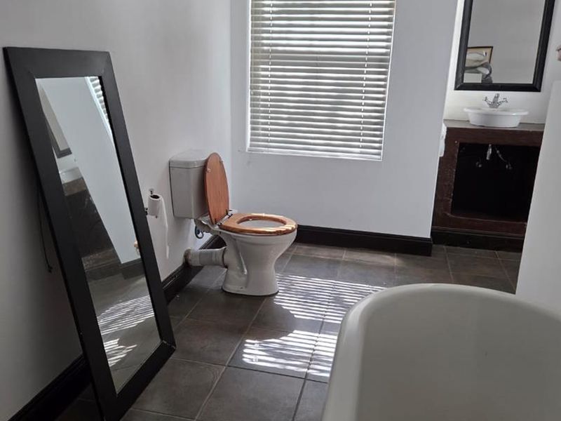 A functional bathroom featuring a freestanding bathtub, a vanity with a vessel sink, and tiled flooring, illuminated by natural light through venetian blinds.