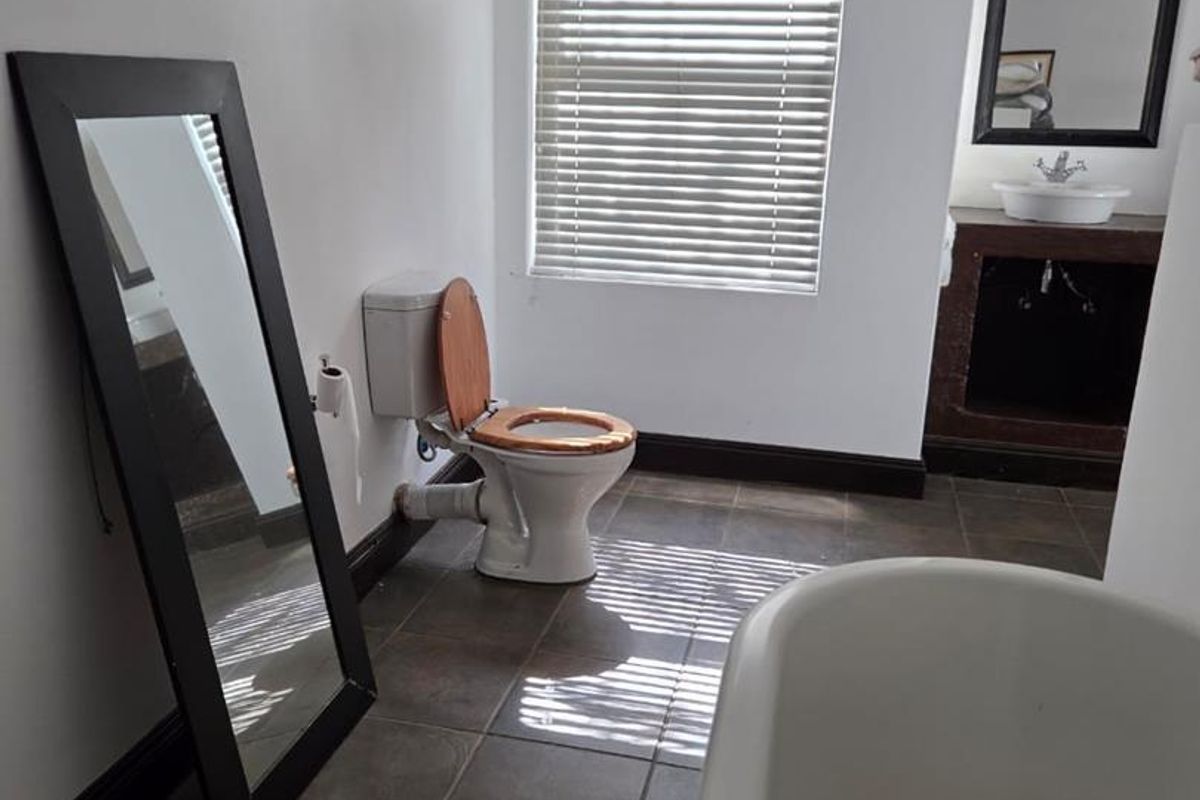 A functional bathroom featuring a freestanding bathtub, a vanity with a vessel sink, and tiled flooring, illuminated by natural light through venetian blinds.
