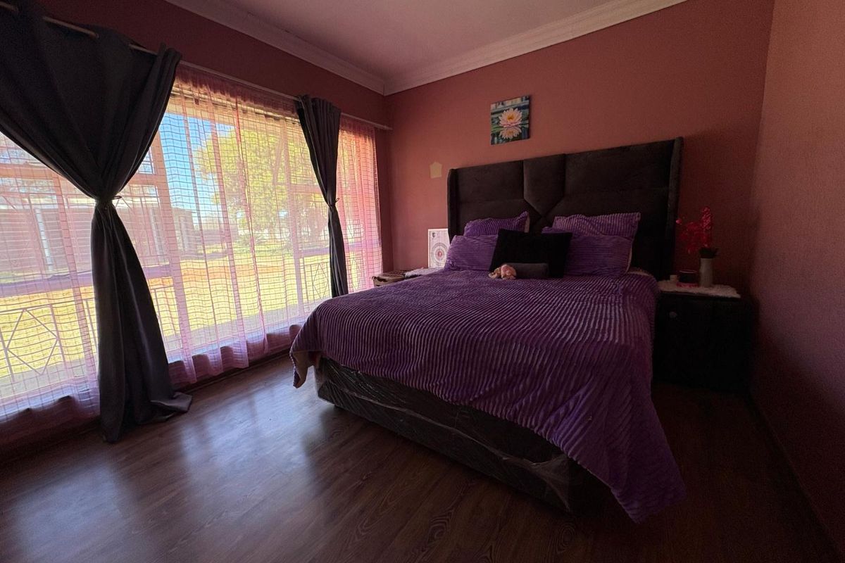 A spacious bedroom featuring wood-look laminate flooring, large windows with security bars, and crown molding.