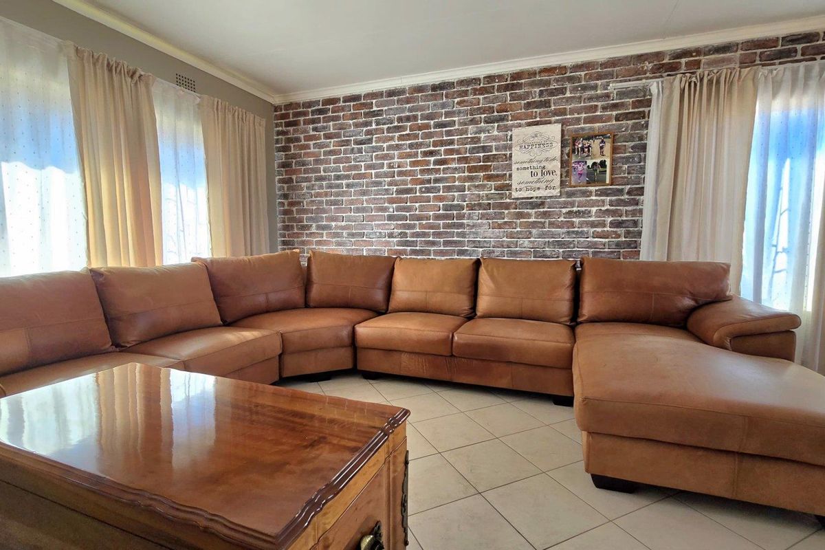 A comfortable living room featuring a distinctive exposed brick feature wall and neutral ceramic floor tiling.