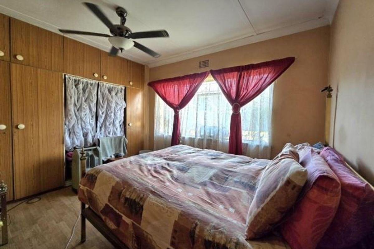 A bedroom featuring built-in wooden wardrobes, a ceiling fan, and large windows with natural light.