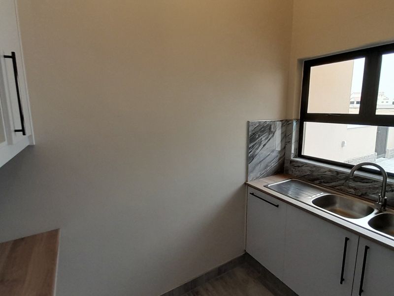 A clean and functional scullery area featuring modern white cabinetry, a stainless steel double sink, and a marble-effect splashback under a window.