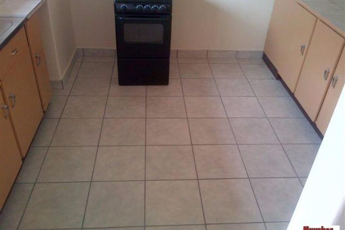 A functional kitchen featuring tiled flooring, wooden cabinetry, and a freestanding electric stove.
