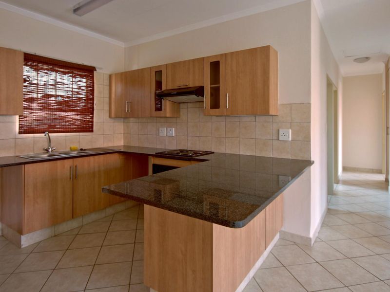 A functional kitchen featuring laminate cabinetry, granite countertops, built-in oven, hob, and extractor fan, finished with ceramic tile flooring and backsplash.