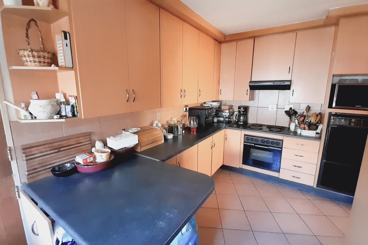 A functional kitchen featuring wood-finish cabinetry, dark countertops, tiled flooring, and built-in oven and hob appliances.