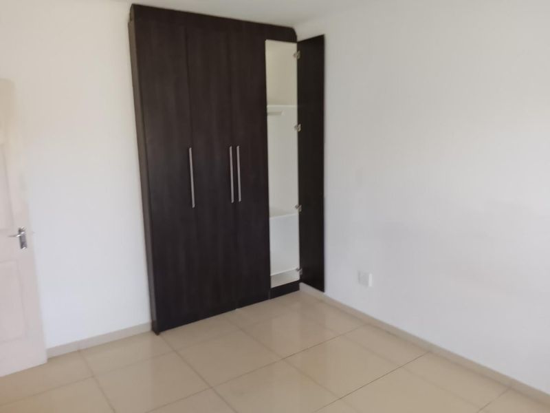 A clean, empty bedroom featuring neutral tiled flooring and dark wood built-in cupboards, offering a blank canvas for personalization.