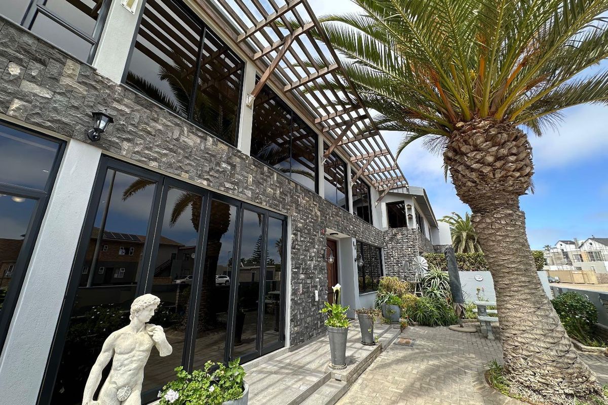 A well-maintained rear exterior featuring stone cladding, large glass sliding doors, and a timber pergola extending over the paved patio area.