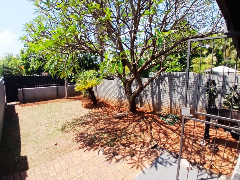 A private rear garden featuring a paved patio area, brick boundary walls with electric fencing, and a large established tree.
