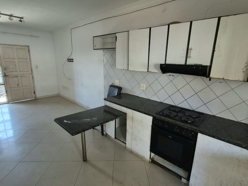 Open plan kitchen and living area featuring tiled floors, built-in cabinetry with granite countertops, and integrated oven and hob.