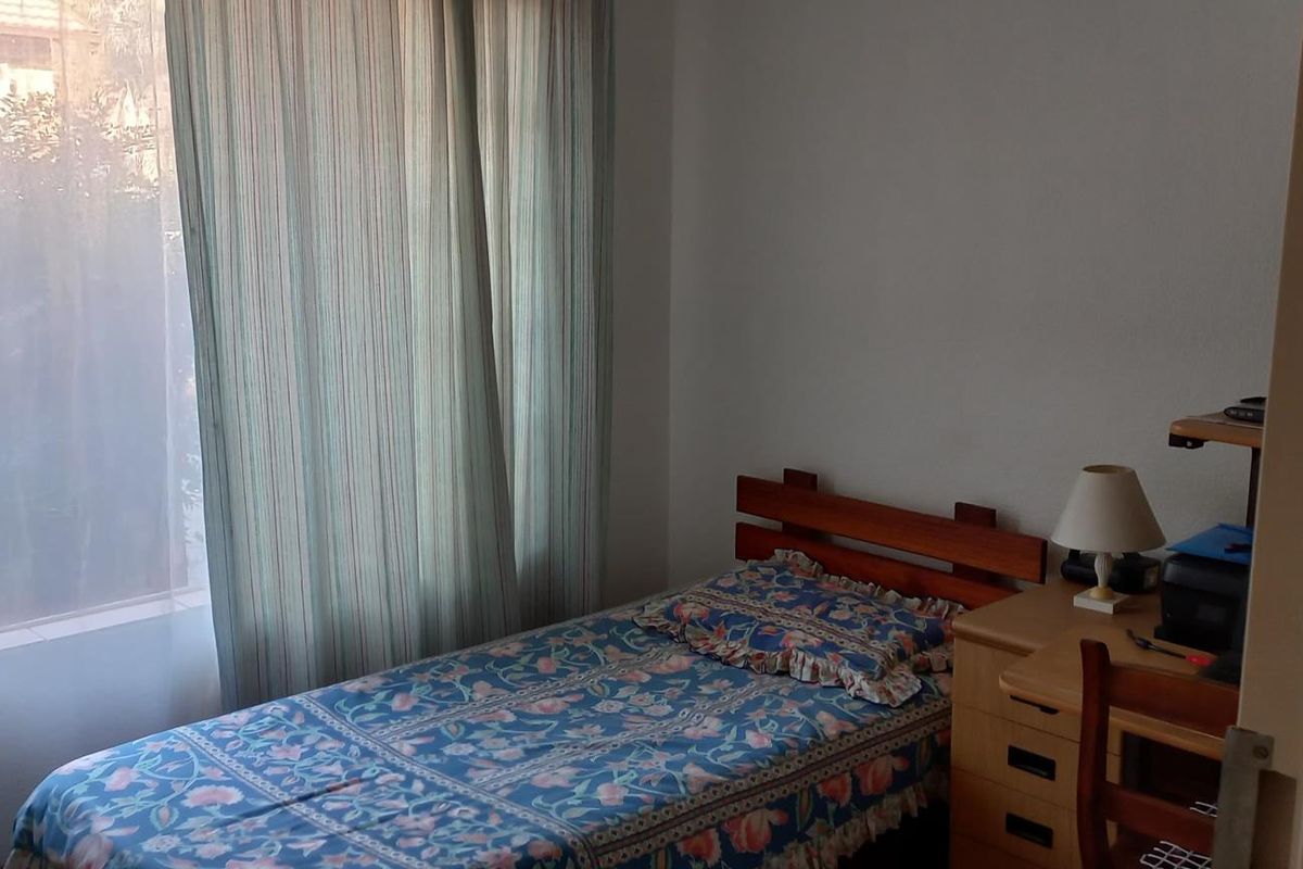 A standard bedroom featuring a large window with floor-to-ceiling curtains, providing natural light and a view of the exterior.