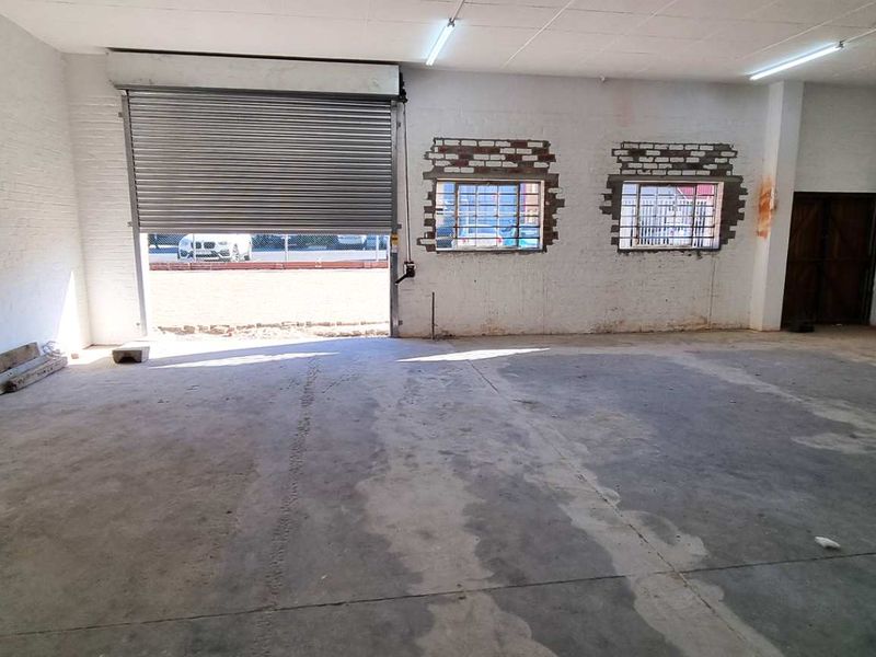 Spacious industrial garage featuring a large roller shutter door, concrete flooring, and exposed brick detailing, suitable for workshop or storage use.